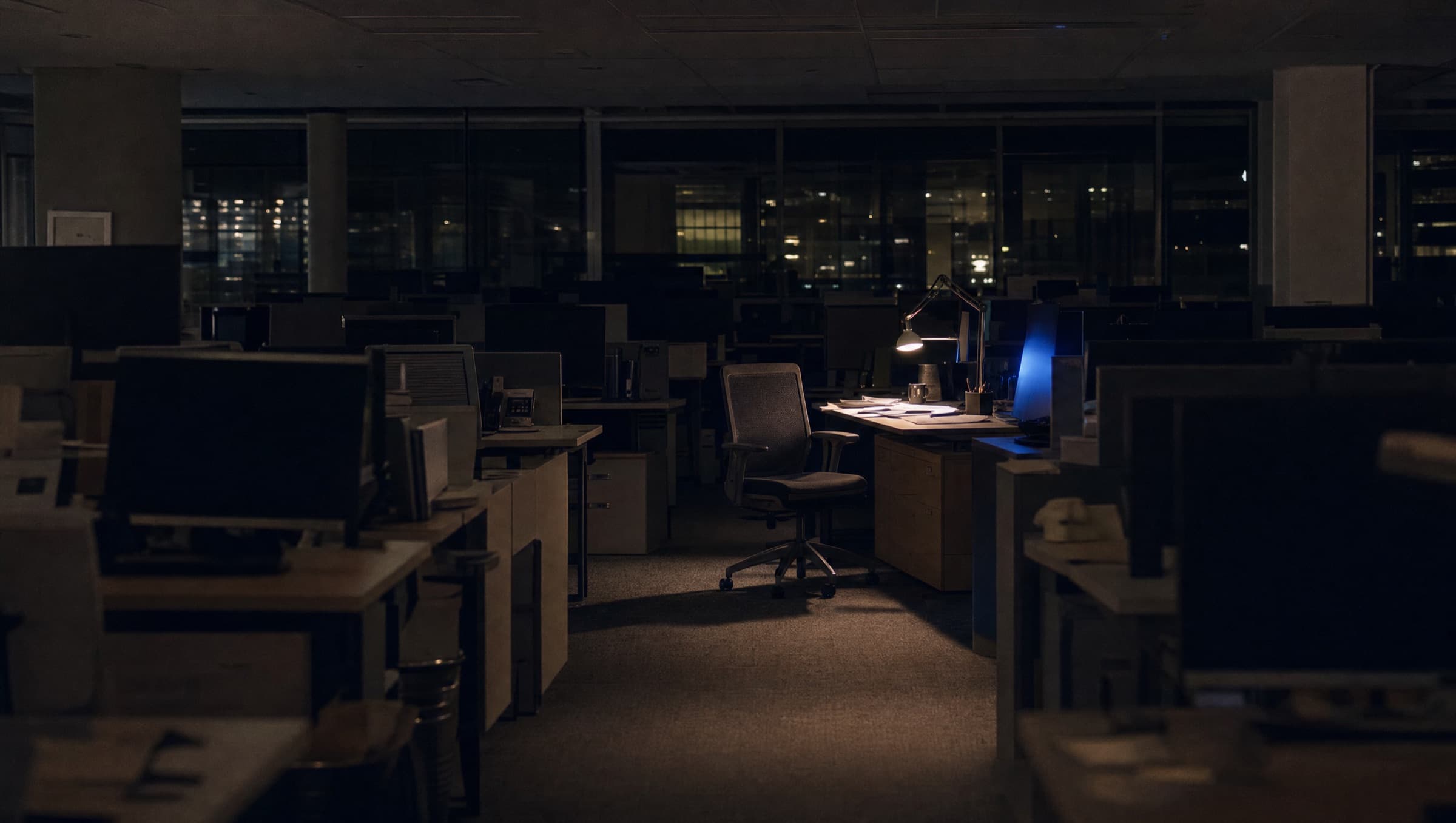 Una oficina abierta de noche con un solo escritorio iluminado y el resto del piso a oscuras