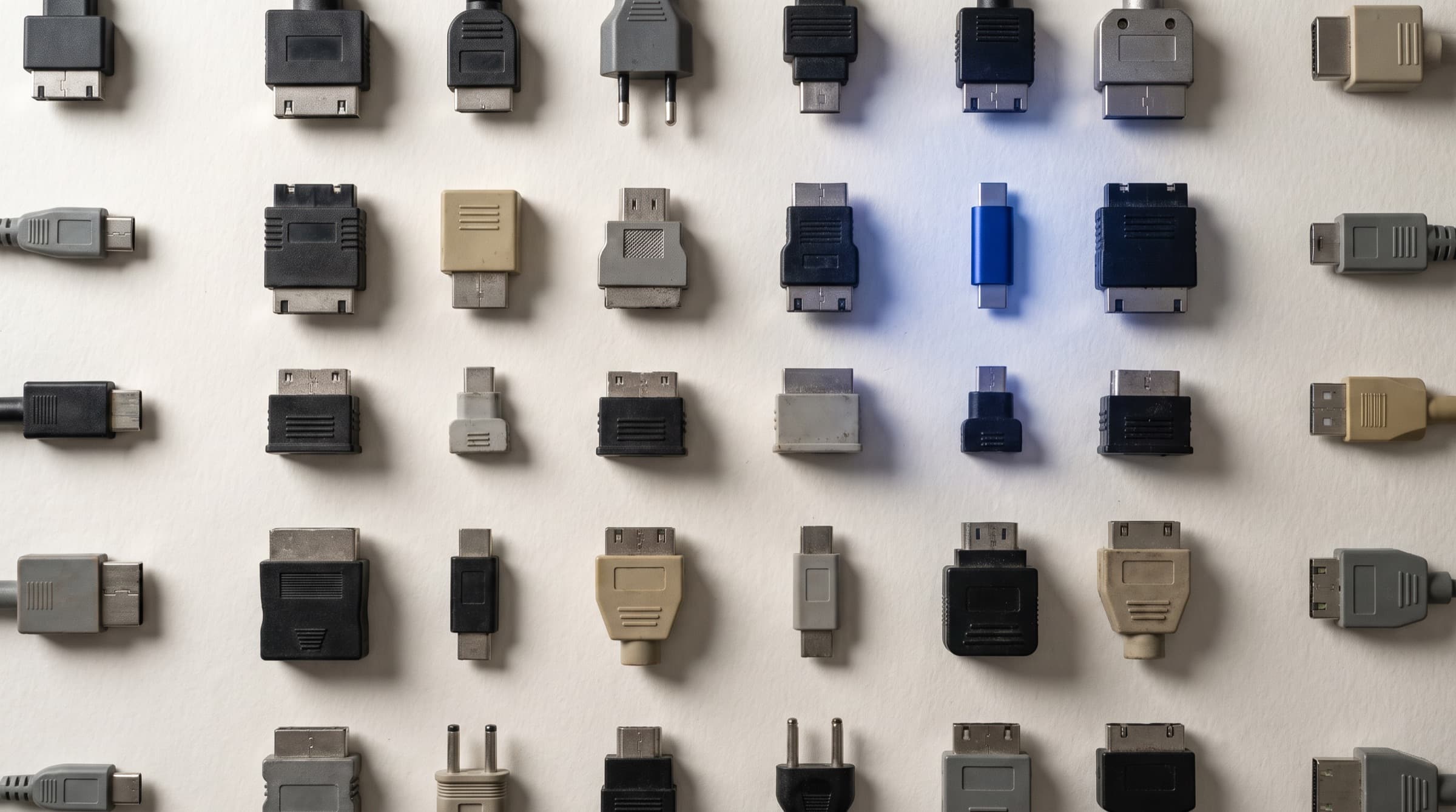 Una cuadrícula de conectores eléctricos disparejos sobre papel color hueso, uno iluminado en azul